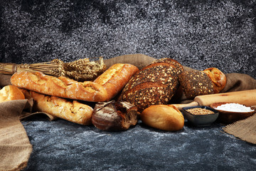 Assortment of baked bread and bread rolls on rustic grey bakery table background