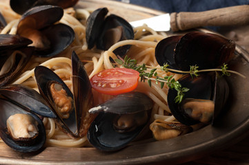 close up of tasty traditional italian pasta and mussels cooked in sauce with tomatoes and rosemary on metal plate