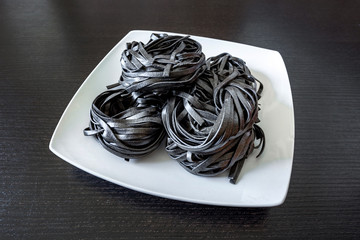 dry black pasta with cuttlefish ink. Pasta of durum wheat semolina with squid ink on a square plate