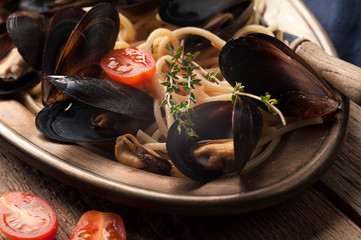 close up of delicious traditional italian spaghetti and mussels cooked in sauce on metal plate with tomatoes on wooden background