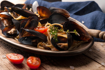 tasty traditional italian pasta and mussels cooked in sauce with tomatoes, rosemary on metal plate near blue napkin on wooden background 
