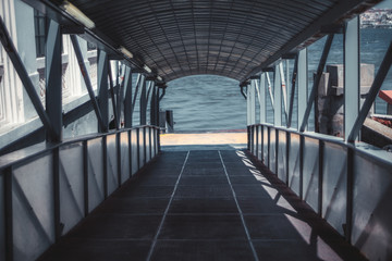 Descending boarding gate covered corridor with plenty of beams, on the quay for passengers of a boat or a ship, with river water in the background, selective focus in a middle, shallow depth of field