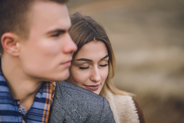 Fototapeta premium A nice beautiful lovely couple in the park or field. man in Gray coat and scarf with girl woman in brown coat. lovers walking hold hands. put her head on his shoulder hugged behind