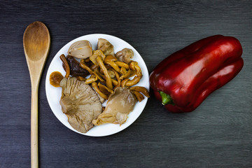 MUSHROOMS IN WHITE PLATE WITH RED PEPPER AND WOODEN SPOON ON DARK WOODEN BACKGROUND