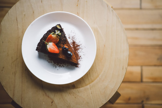 One piece of vegan raw chocolate avocado brownie cake on wooden table. Sugar free, wheat free, dairy free, flourless dessert. Dark mood food photo, blogging. Healthy eating, lifestyle concept