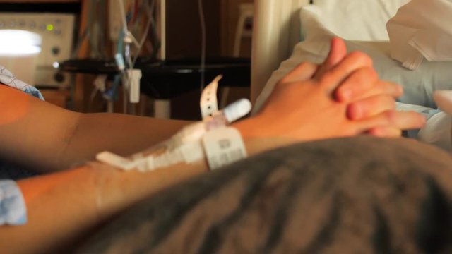Womans Hands Clasped On Hospital Bed With Iv At Sunset. Woman clasps her hands together while laying on hospital bed.