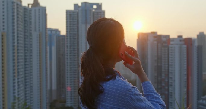 Woman talk to cellphone in the background of the city under sunset time