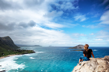 Fototapeta na wymiar Woman sitting atop a cliff overlooking Oahu, Hawaii's south shore