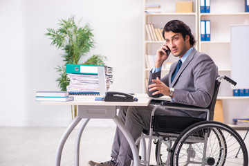 Young handsome employee in wheelchair at the office 