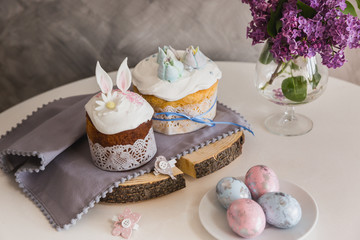 Easter Cakes on wooden decorated with rabbit ears, eggs on whith plate on foreground, lilac on background. - Traditional Kulich, Paska Easter Bread
