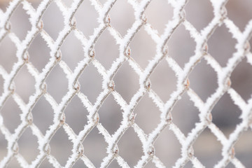 Naklejka premium Abstract background of wire fence in winter, covered with frozen snow and ice. Shallow depth of field, blurred background