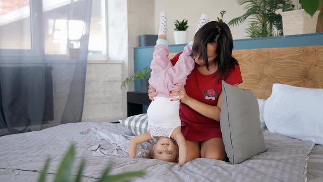 Happy family moment between little daughter and young mother in bedroom.