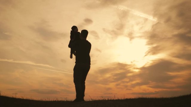 Silhouettes father and little son playing on the meadow at the sunset time. Concept of friendly family.