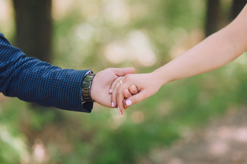 Hands newlyweds on nature close-up. The groom with the clock holds the bride by the hand with a wedding ring. Gentle wedding photo.