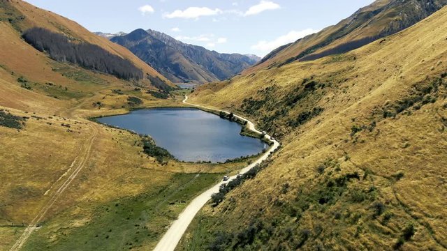 Cinematic 4k aerial drone footage stopping near lake moke and circling around car showcasing beautiful landscapes, mountains and lakes in the background in queenstown new zealand glenorchy road