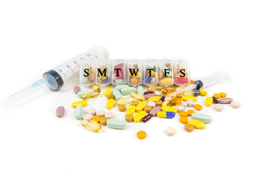 Multicolored pills in and around a large syringe and daily pill planner