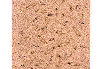 Gold safety pins spread out on a piece of cork board