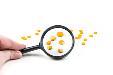 Hand holding a black magnifying glass looking at pills