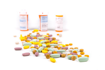 Pile of green orange purple and yellow pills in front of prescription bottles