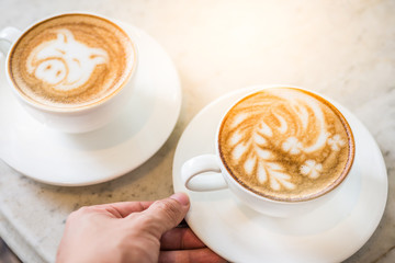 Two cups of coffee with beautiful leaf and pig latte art and sun flare lighting on a marble table in a coffee shop in the morning.