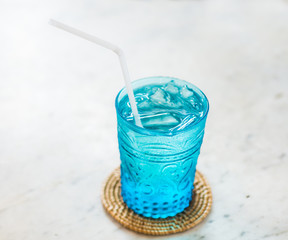blue glass of cold water and plastic straw on the marble table , feel freshness