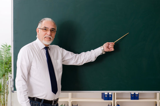 Aged male teacher in front of chalkboard