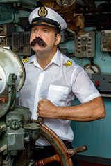 A sailor officer - old salt in the uniform is steering the ship with a rudder. Captain standing in the wheelhouse of ship and looking ahead. © milkovasa