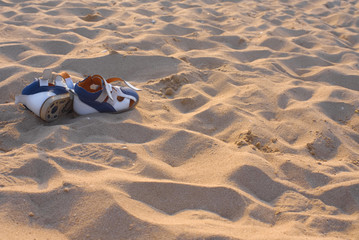 Obraz premium Blue-orange sandals on a sandy ocean beach on a sunny day