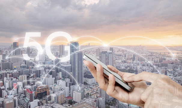 Hand using mobile smart phone, and wireless network connection technology in the city, with 5g internet networking sign