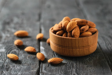 Wooden bowl with almonds on black wooden table.