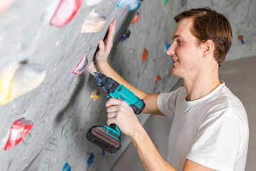 Rock climber fastens the hook with a screwdriver at the climbing wall in the boulder hall © Baikal360