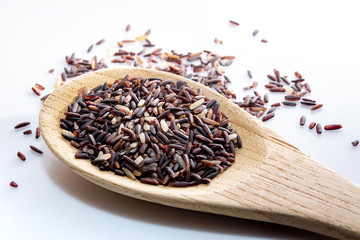 Brown rice, riceberry organic food in a wooden spoon on white background
