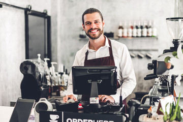 Portrait of handsome bearded barista man small business owner smiling behind the counter bar in a...