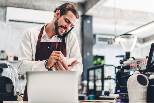 Portrait Of Handsome Bearded Barista Man Small Business Owner Smiling And Receive Order From Customer Behind The Counter Bar In A Cafe