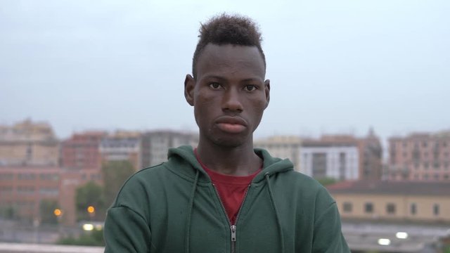 Serious confident young black african migrant staring at acmera-outdoor