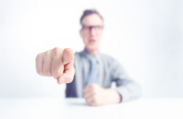 Businessman sitting at the table points a finger at you, shallow depth of field. Concept of evil boss. 