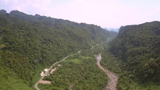 narrow mountain brooklet winds across amazing tropical green valley near small asphalt road upper view