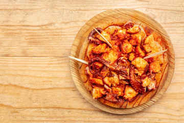 Pulpo a la gallega, an octopus with boiled potatoes and paprika, typical Spanish Galician dish, on a traditional wooden plate, shot from above on a wooden background with a place for text