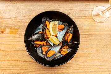 Mussels with lemon slices and a glass of wine, shot from the top on a wooden background with a place for text
