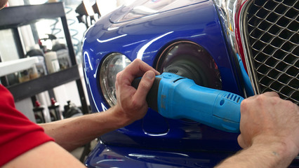 Closely shown as a professional worker polishes the transport (car) body using a polishing tool (machine). Concept from: Auto service, Car Painting, Machine washing.	