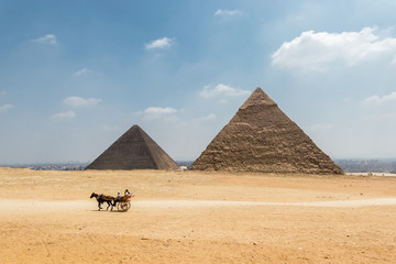 Fototapeta na wymiar Horse carriage with tourists in front of the Pyramid of Khufu and the Pyramid of Khafre in Egypt