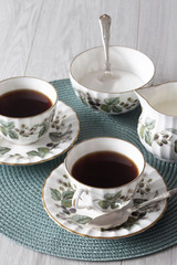 Cup of tea on saucer with teaspoon milk jug and sugar bowl on a green placemat with grey wood surface