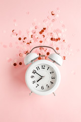 Top view white alarm clock covered golden confetti on pink background. Template feminine blog social media. Minimal style. flat lay