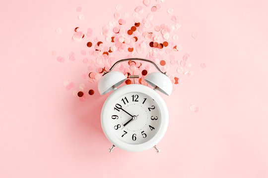 Top view white alarm clock covered golden confetti on pink background. Template feminine blog social media. Minimal style. flat lay