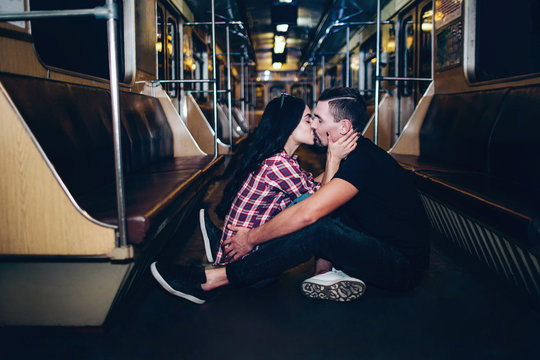 Young man and woman use underground. Couple in subway. Lovely cheerful couple sit together on floor and kissing. Alone in empty underground carriage. Love story. Urban modern view.