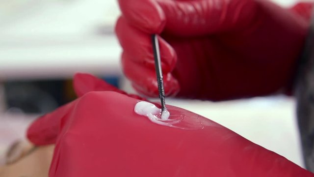 Close-up of the hands of the master of the beauty salon in red rubber gloves, applying the dye. Cosmetician does permanent makeup eyelashes