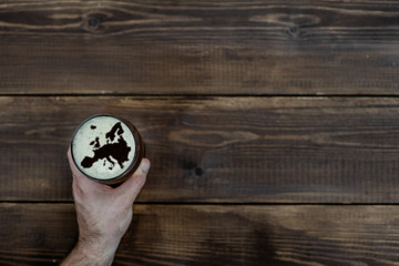 man's hand holds a mug of dark beer with silhouettes of Europe on foam. Top view. Empty space for text