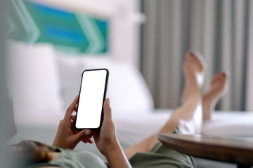Mockup image of a woman holding and using mobile phone with blank screen while relaxing and lying on the bed