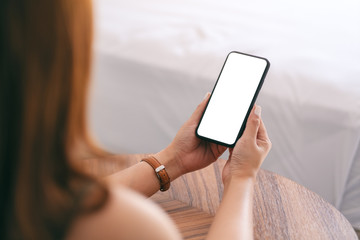 Mockup image of a woman holding and using mobile phone with blank screen while sitting beside the...