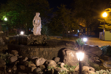 Statue of a girl next to a creek in a city park with night illumination.